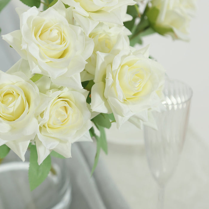 Artificial white roses in a decorative arrangement with champagne flutes.