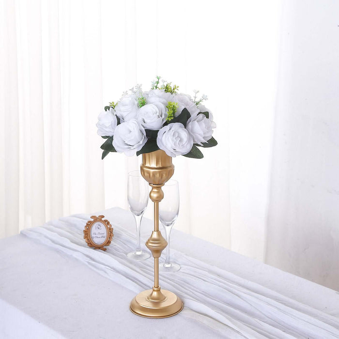 Gold flower vase with white roses and greenery on a table.