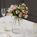 Artificial flower bouquet in a clear glass vase on a dining table.