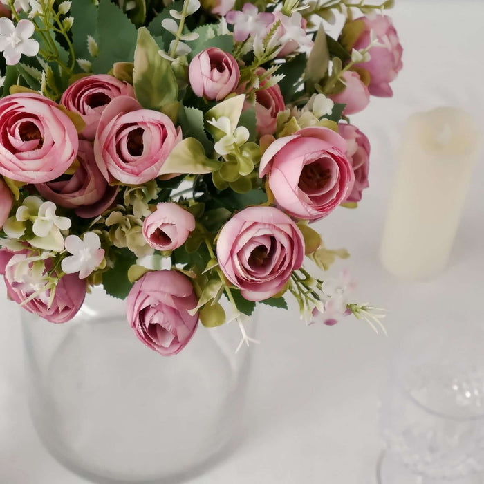 Pink rose bouquet in a glass vase with greenery and a candle in the background.