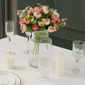 Elegant floral centerpiece with pink roses in a glass vase on a dining table.