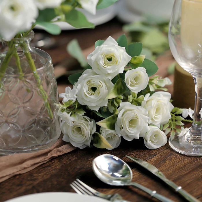 White roses bouquet on a rustic table setting with glassware and cutlery.
