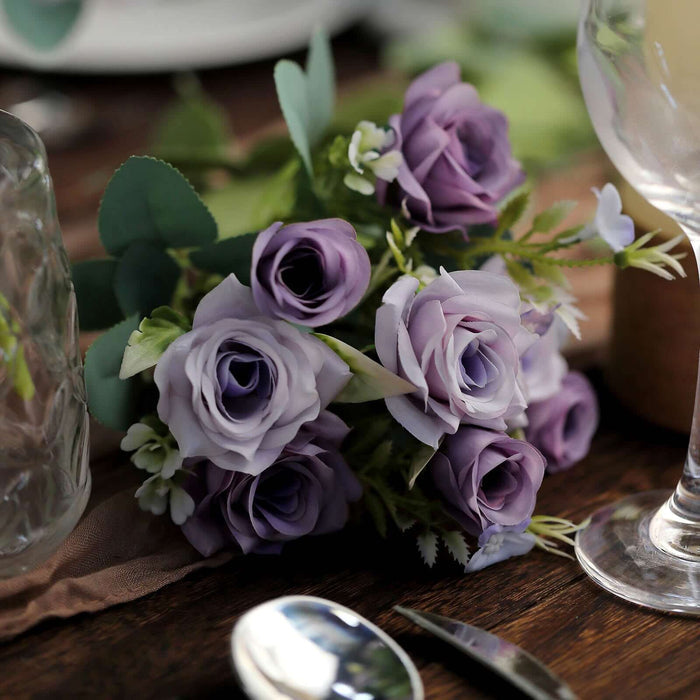 Purple artificial rose bouquet with greenery on wooden table.
