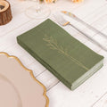 Green napkins with gold leaf design set on a rustic table setting.
