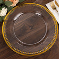 Clear glass charger plate with gold beaded rim on a wooden table setting.
