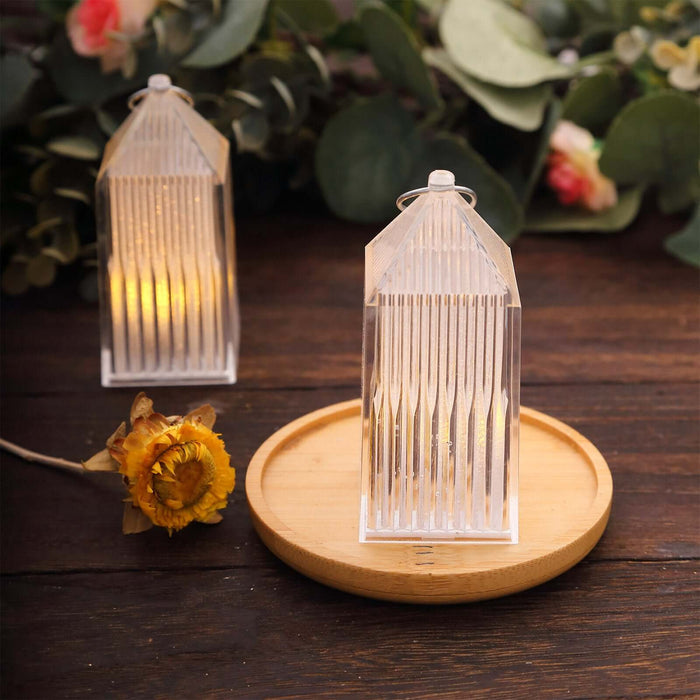 Clear geometric lanterns on a wooden tray with greenery backdrop.
