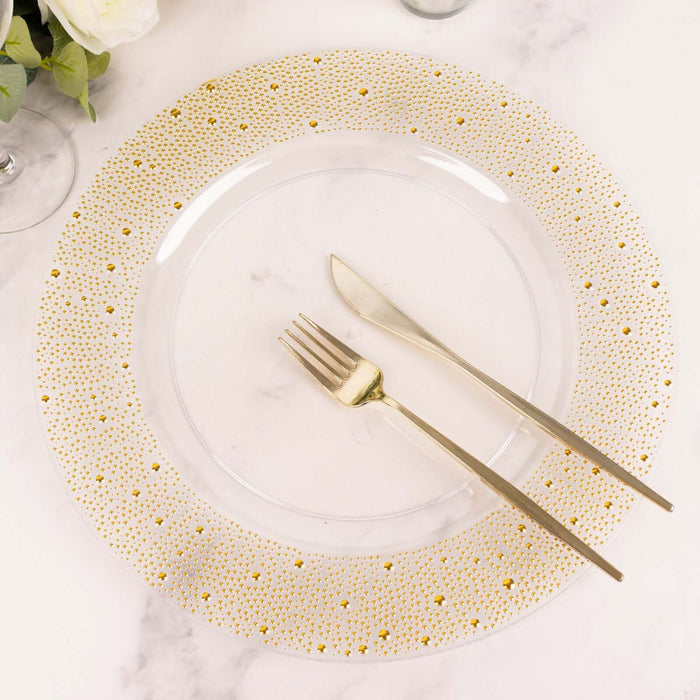 Clear plate with gold-dotted rim, gold fork and knife on marble surface.