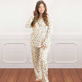 Woman wearing a pajama set with holly and red bows in a room with wooden flooring and white paneled walls.