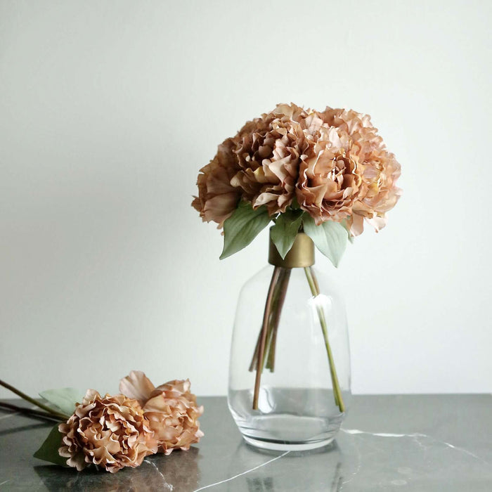 Peach-colored flowers in a clear vase on a marble surface.
