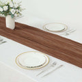 Brown table runner on a white table setting with plates and silverware.