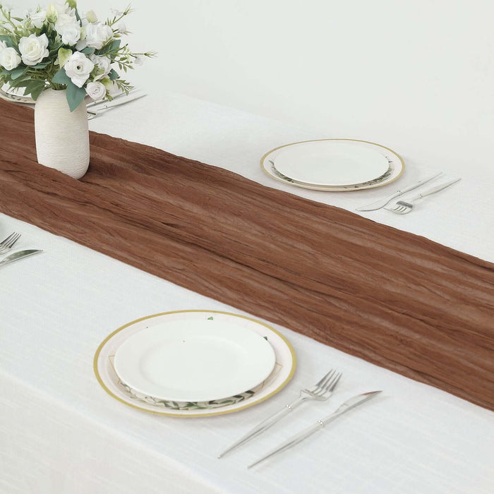 Brown table runner on a white table setting with plates and silverware.