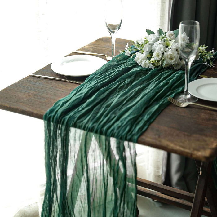 Green table runner draped over a wooden table with white plates and floral arrangement.