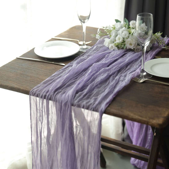 Purple table runner draped elegantly over a wooden table with tableware and flowers.