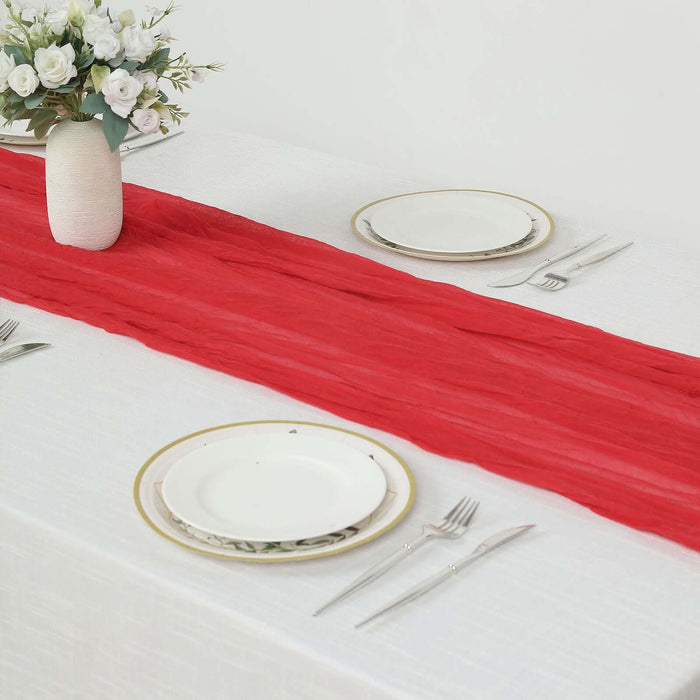 Red table runner on a white table setting with plates and cutlery.