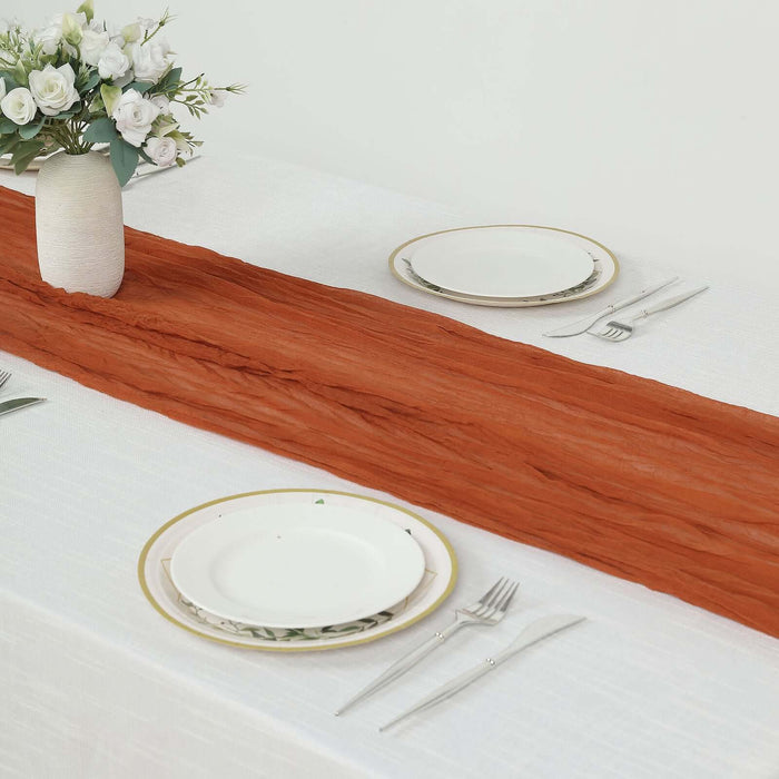 Rust-colored table runner on a white dining table with plates and silverware.