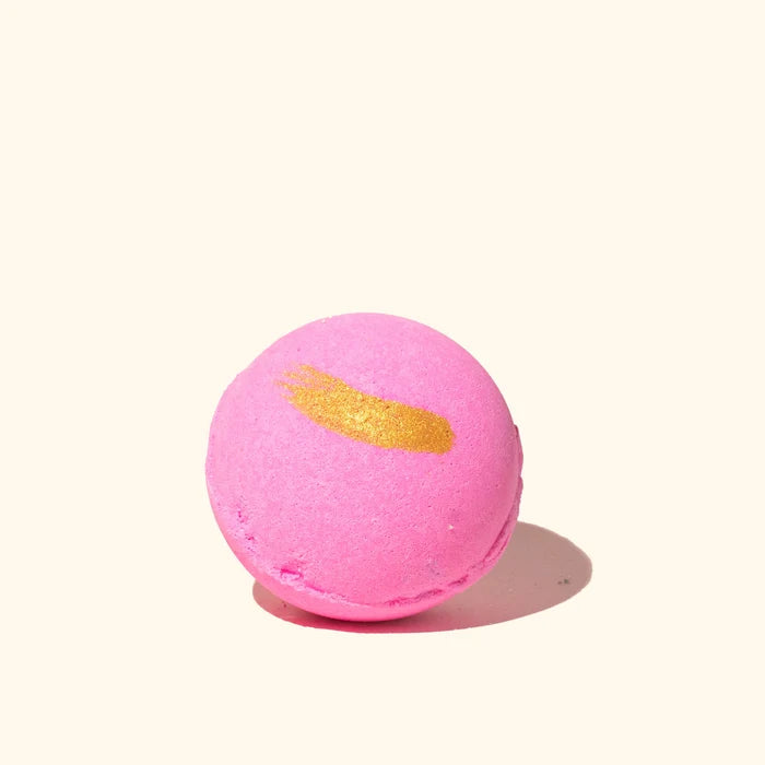 Pink bath bomb with a gold accent on a white background