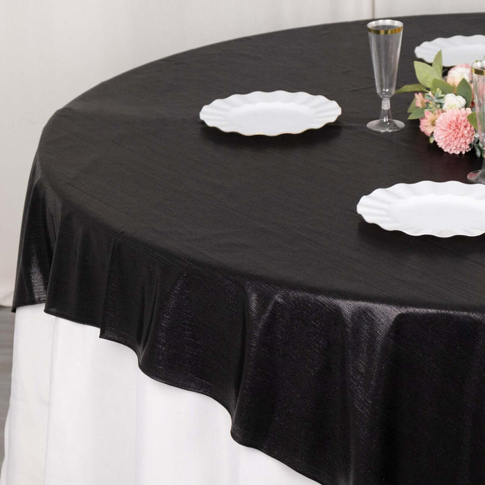 Black tablecloth draped over a round table with white plates and floral centerpiece.