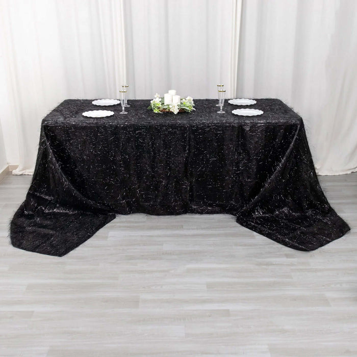 Black textured tablecloth draped over a table with candles and plates.