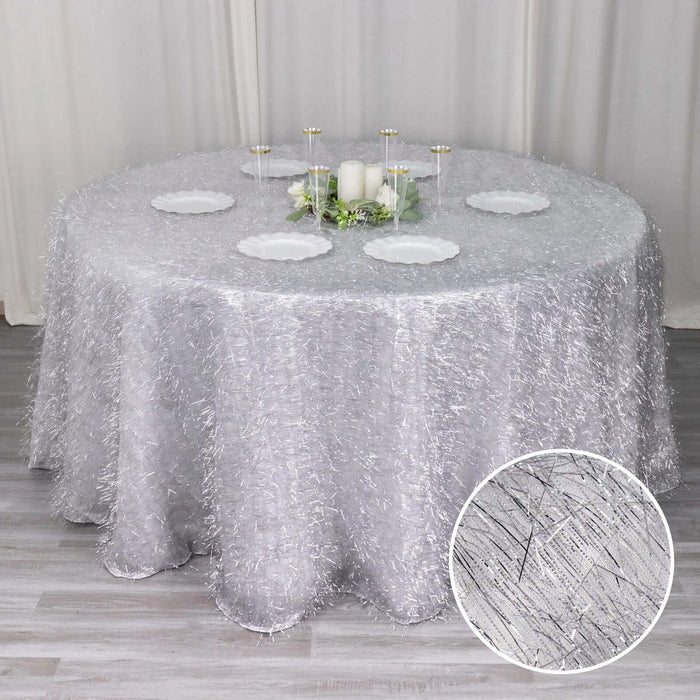 Silver textured tablecloth on a round table with decorative plates and candles.