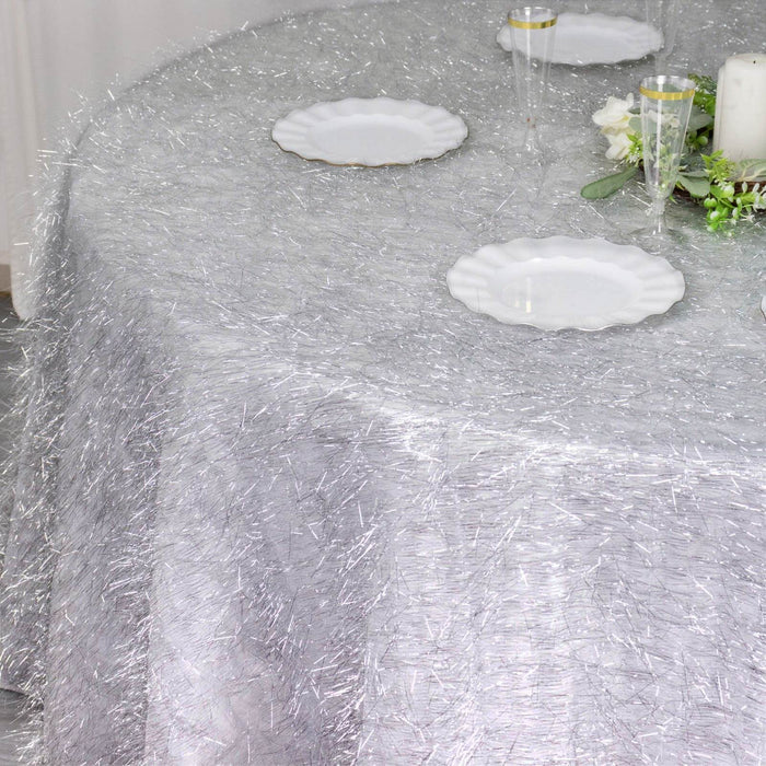 Silver textured tablecloth on a round dining table with white plates and decor.