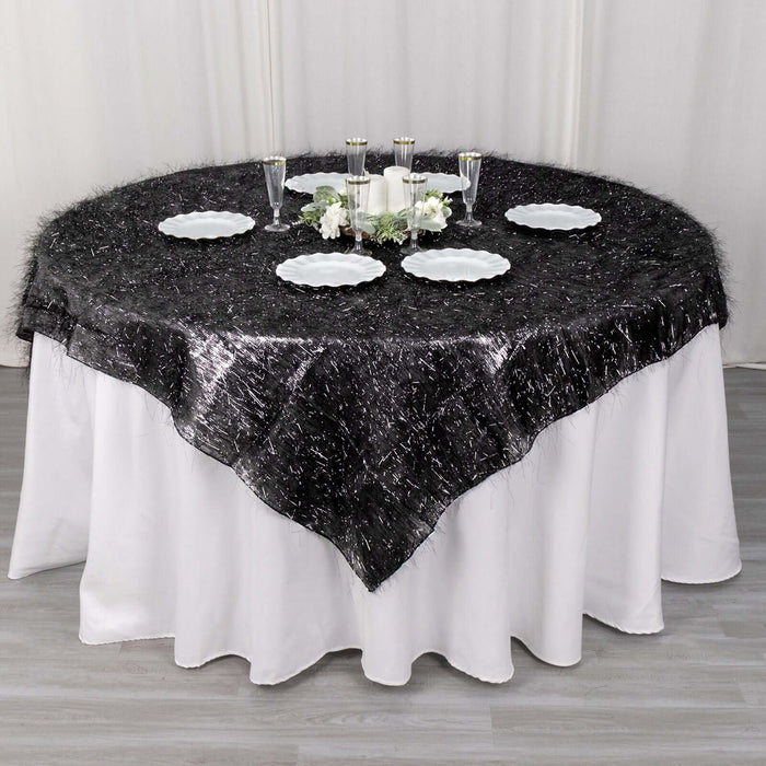 Black and silver textured tablecloth on a round table with white plates and decorations.