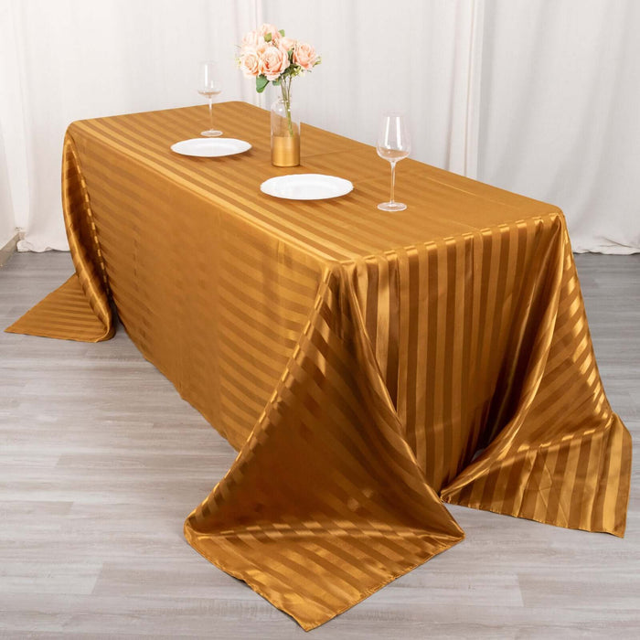 Elegant gold striped tablecloth draped over a table with floral centerpiece and glasses.