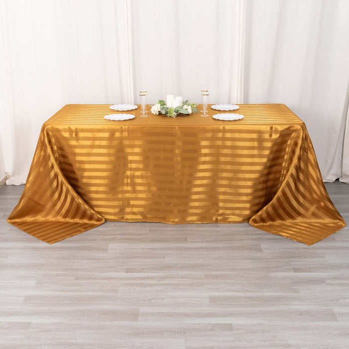 Gold striped tablecloth on a dining table with decorative plates and candles.
