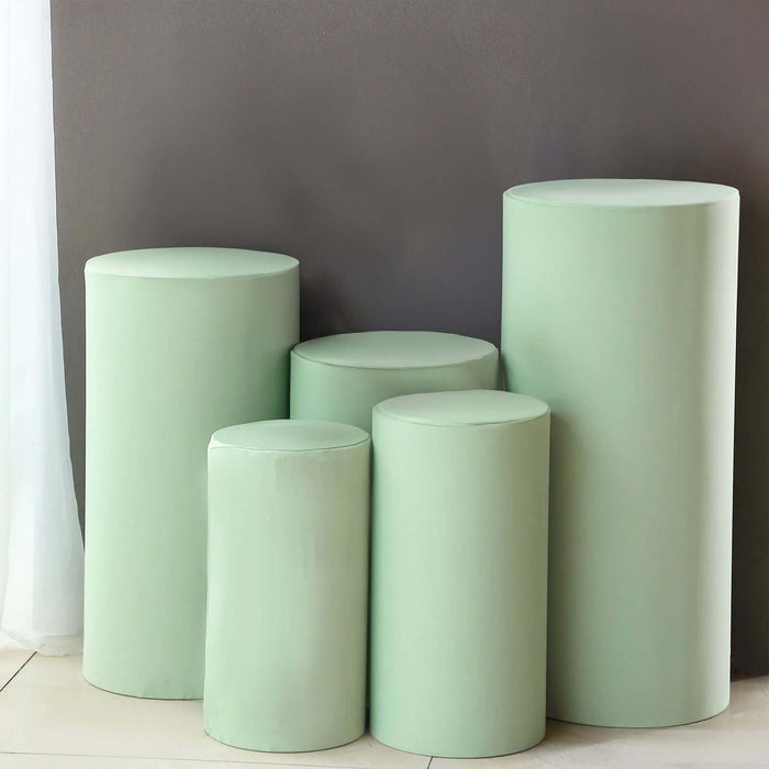 Green cylindrical pedestals in various sizes against a gray wall.