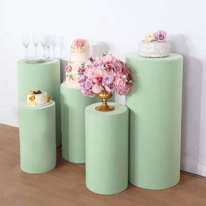 Green display pedestals with cakes and floral arrangements.