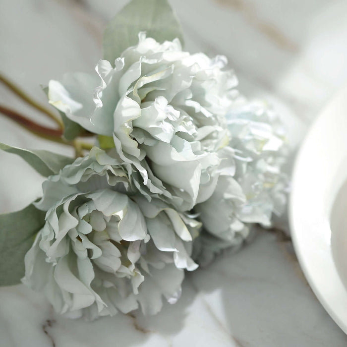 Artificial light blue peony flowers on a marble surface.