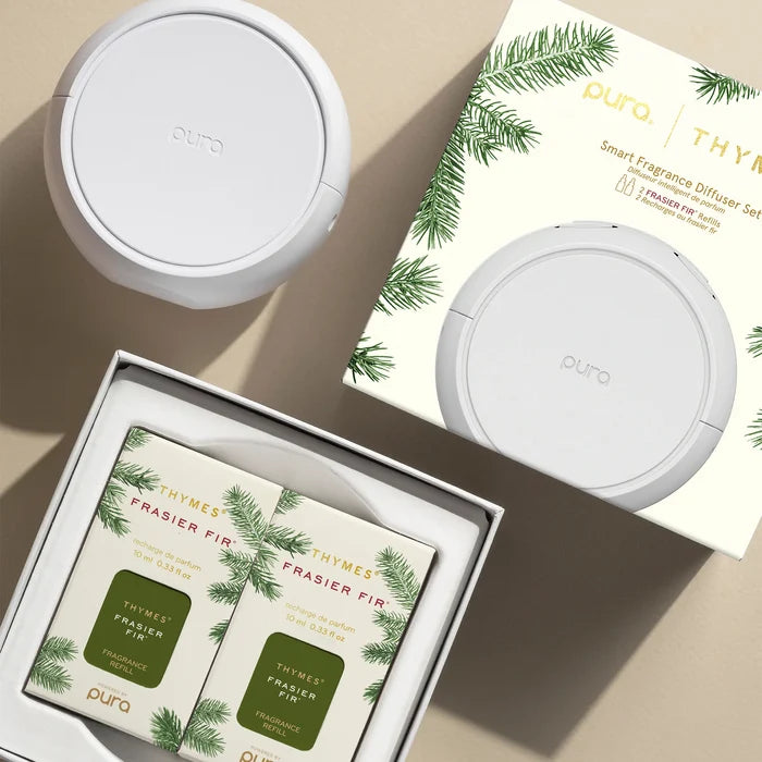 Pura Thymes Frasier Fir smart fragrance diffuser set, featuring two white diffusers, their illustrated packaging box, and an open tray containing two matching sachets with pine green illustrations.