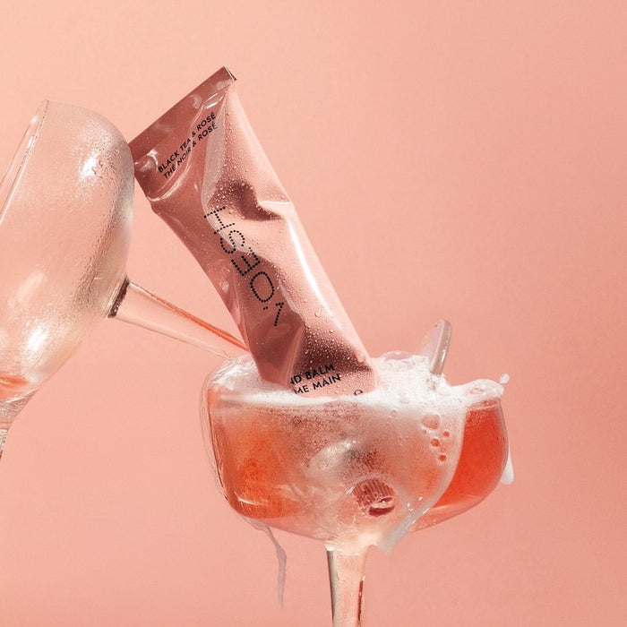 VOESH hand balm Black Tea & Rosé being poured into a cocktail glass with ice against pink background