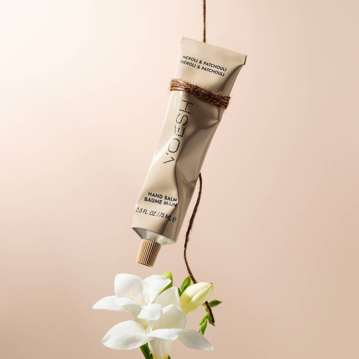 VOESH hand balm with neroli and patchouli hanging from twine above white flowers on beige background